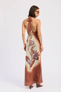 Woman wearing a long, patterned dress with a halter neck design on a white background