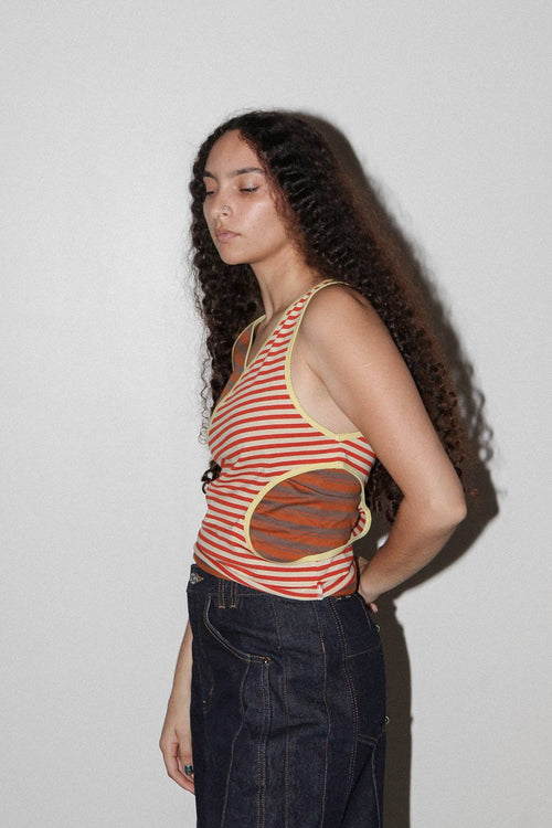 Woman wearing a red and white striped tank top with a graphic design, standing against a plain background.
