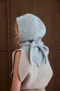 Person wearing a light gray knitted hood with a bow on a wooden background