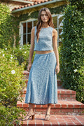 Woman in a blue textured outfit standing on a brick step outdoors.