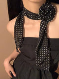 Person wearing a black polka dot scarf with a flower accessory on a beige background