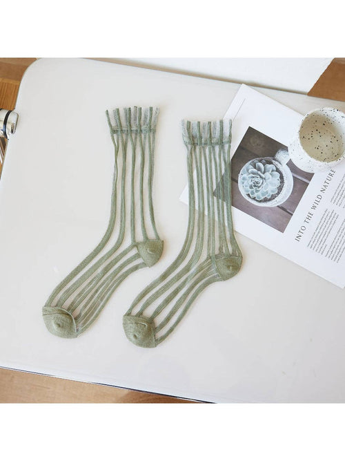 Pair of green striped socks on a white surface with a magazine underneath.