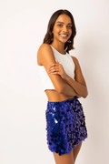 A woman posing in a white sleeveless crop top and a vibrant blue sequined mini skirt against a plain white studio background.