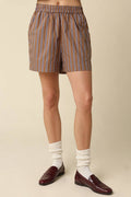 Person wearing striped shorts, white socks, and brown shoes on a beige background