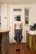 Person standing in a kitchen doorway wearing a white top and gray skirt.