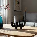 Black candle holder with a lit candle on a wooden table in a living room setting.