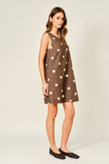 Woman wearing a brown dress with white polka dots on a plain background