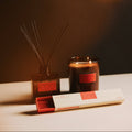 Candle, diffuser, and packaging on a table with a warm glow