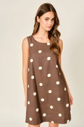 Woman wearing a brown dress with white polka dots on a plain background