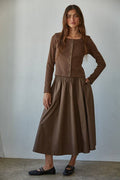 Woman wearing a brown outfit with a long skirt and top against a plain background