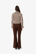 A model viewed from the back wearing a brown and beige vertically striped long-sleeve blouse with ruffled cuffs and dark brown flared trousers, set against a plain light gray background.