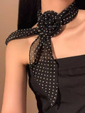 Black polka dot scarf tied around a person's neck against a neutral background