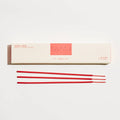 Red incense sticks in front of a white box with red label on a white background