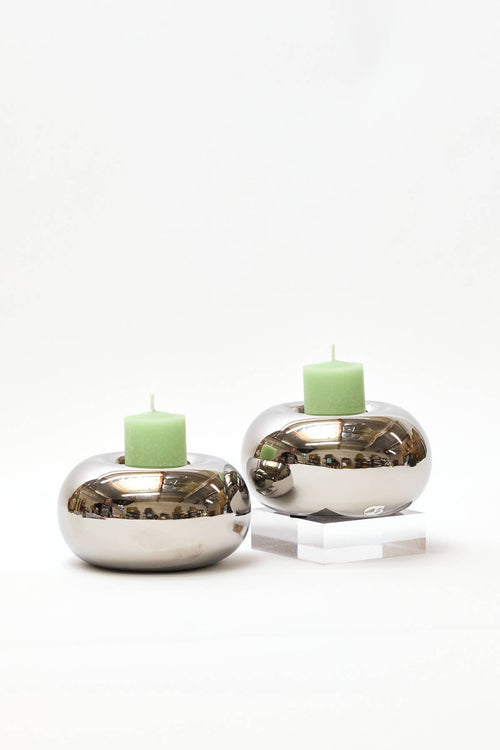 Two silver candle holders with green candles on a white background