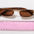 Sunglasses with gold frame and tortoiseshell pattern next to a pink ruler on a white background