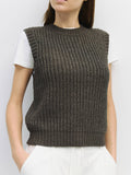 Person wearing a brown knitted vest over a white shirt on a plain background