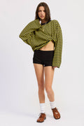 Woman wearing a yellow and black striped sweater with black shorts on a white background