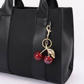 Black handbag with a cherry keychain on a light gray background