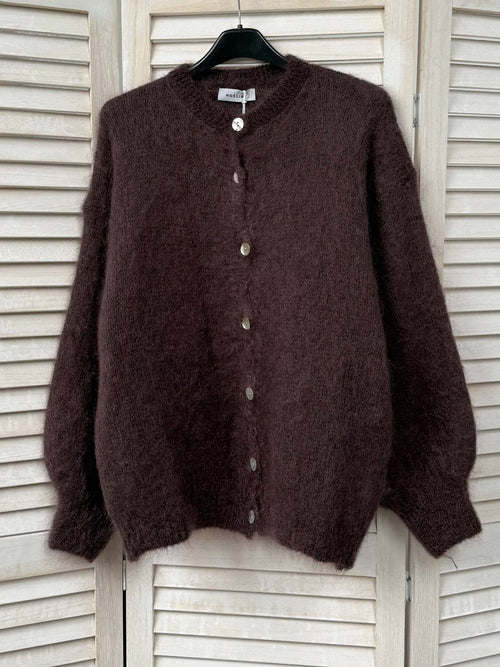 Brown cardigan on a hanger against a white wooden panel background