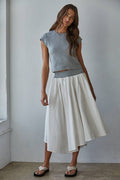 Woman wearing a gray top and white skirt against a plain background