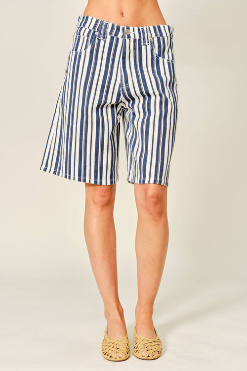 A person wearing blue and white vertically striped denim shorts, paired with tan woven flat shoes, photographed against a plain light beige studio background.