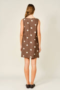 Woman wearing a brown dress with white polka dots on a plain background
