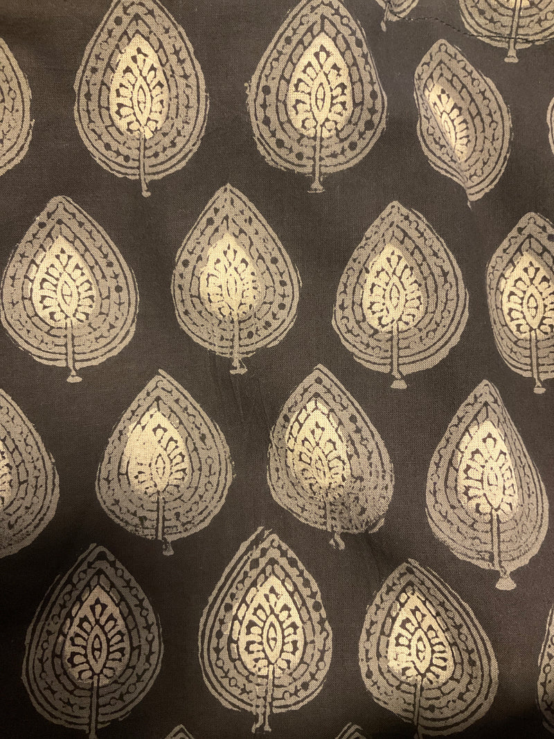 A close-up of a dark brown or charcoal fabric with a repeating metallic gold leaf block-print pattern.