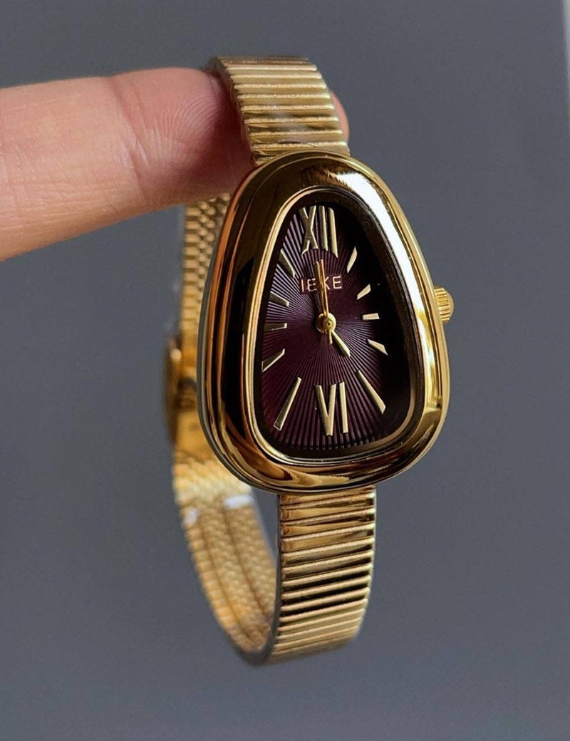 Gold watch held by a finger against a gray background