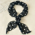 Black polka dot scarf tied into a bow on a beige background with lace trim.