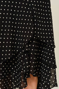 Black polka dot dress with ruffled layers on a neutral background