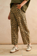 Person wearing leopard print pants and green top against a beige background