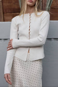 Woman wearing a white ribbed sweater with a wooden fence and cactus in the background