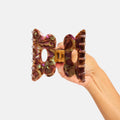 Hand holding a bow-shaped hair clip with a marbled design on a light gray background