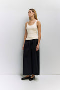 Woman wearing a white tank top and black wide-leg pants against a white background