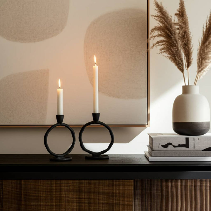 Decorative setup with candles in black holders, a vase with dried plants, and books on a wooden surface.