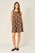 Woman wearing a brown dress with white polka dots on a plain background