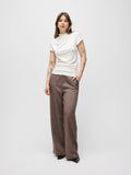 A model stands against a light gray studio background wearing a white short-sleeve mock-neck top and brown pinstriped wide-leg trousers.