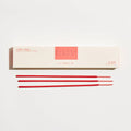 Red incense sticks in front of a white box with 'P.F. Candle Co' branding on a light gray background