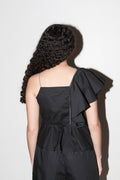 Person wearing a black outfit with a ruffled shoulder against a white background