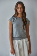 Woman wearing a gray top and white skirt against a plain background