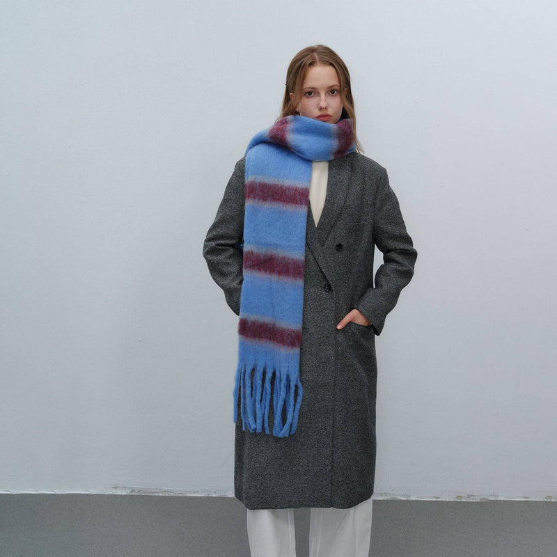 Person wearing a long gray coat and a blue scarf with red stripes against a plain background