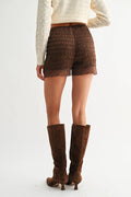 Person wearing brown textured shorts and knee-high boots on a white background