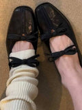 Black shoes with black bows worn with white socks on a textured surface