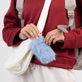 Person holding a blue fluffy keychain with a white bag and red jacket.