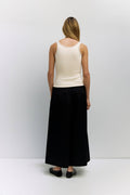 Person wearing a white tank top and black wide-leg pants on a plain background