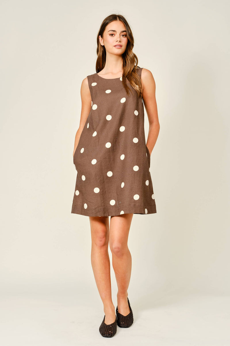 Woman wearing a brown dress with white polka dots on a plain background