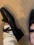 Black shoes with bow details worn with white socks on a textured surface