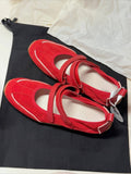 Red ballet flats on a black shoe bag with a white background
