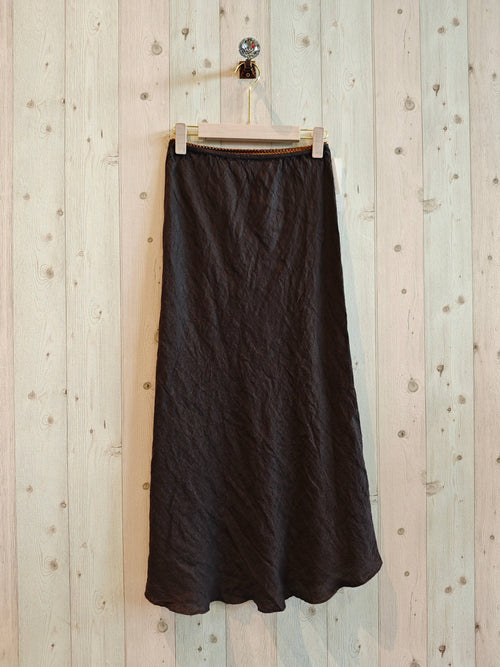 Black skirt hanging on a wooden hanger against a light wooden panel background