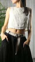 Person wearing a white sleeveless top and black pants with a belt, standing indoors.